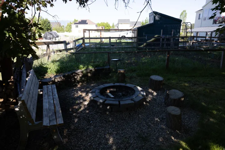 Outdoor fire pit area with gravel groundcover, wood-plank bench seating, and tree stump accents