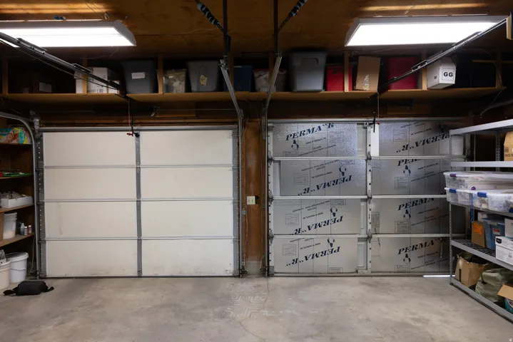Two-car garage featuring a concrete floor, overhead fluorescent lighting, and accessible storage shelving