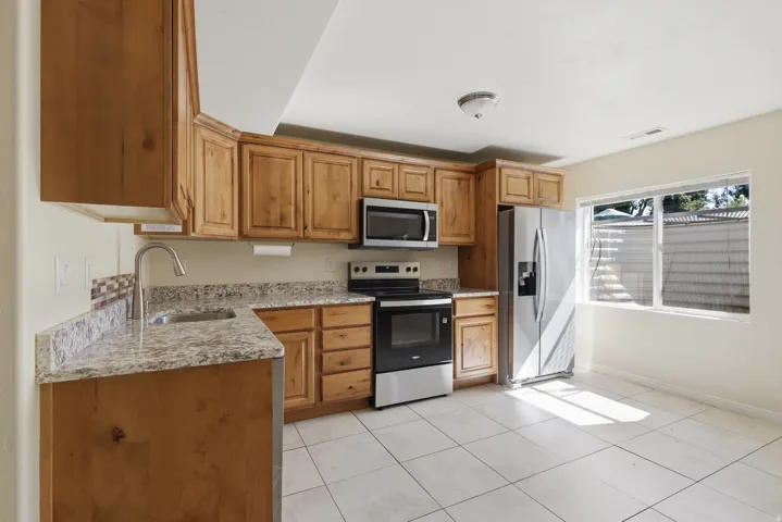 Kitchen featuring wood cabinetry, granite-finish countertops, stainless steel appliances, and tile flooring