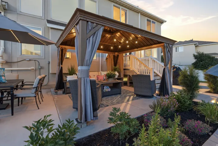 Outdoor living space featuring a pergola with string lights, concrete patio, and landscaped garden beds