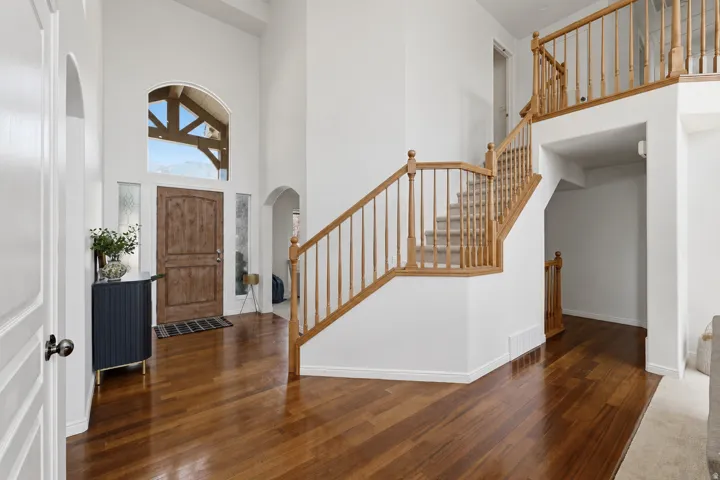 Two-story entryway featuring wood-finish flooring, a grand staircase with wood balusters, and a vaulted ceiling with an arched window