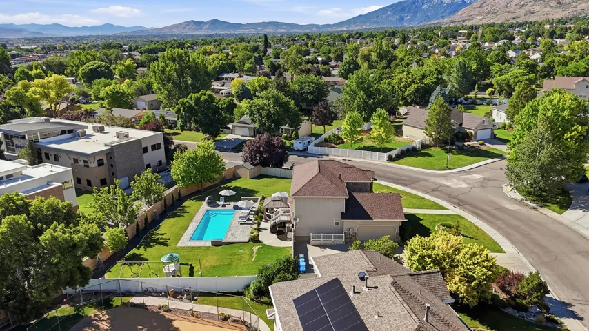 Expansive backyard featuring a fenced-in swimming pool with surrounding patio, mature trees, and a manicured lawn