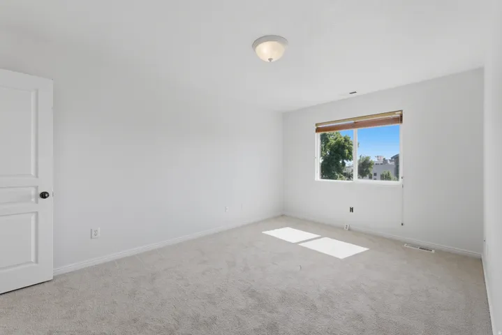 Carpeted room featuring a white interior door with dark hardware, a flush-mount ceiling light fixture, and a window with wood-finish blinds offering exterior views