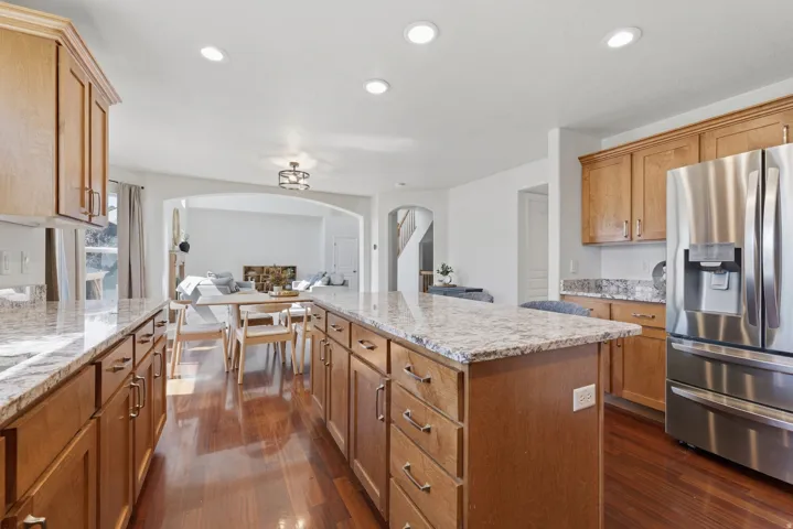 Kitchen featuring a central island with a light-toned countertop, wood-finish cabinetry, stainless steel refrigerator, recessed lighting, and wood-finish flooring