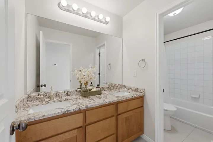 Bathroom featuring a dual vanity with light-toned cabinetry, a speckled countertop, and two undermount sinks