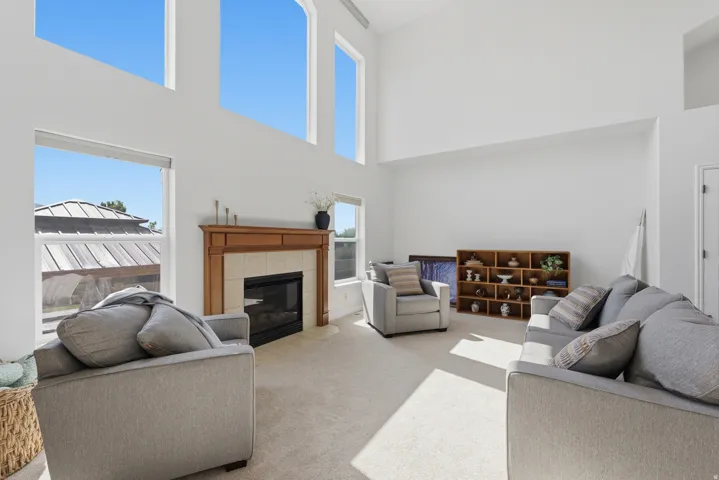 Two-story living area featuring a fireplace with a wood mantle and tile surround, arched windows, light-colored carpeting, and white walls