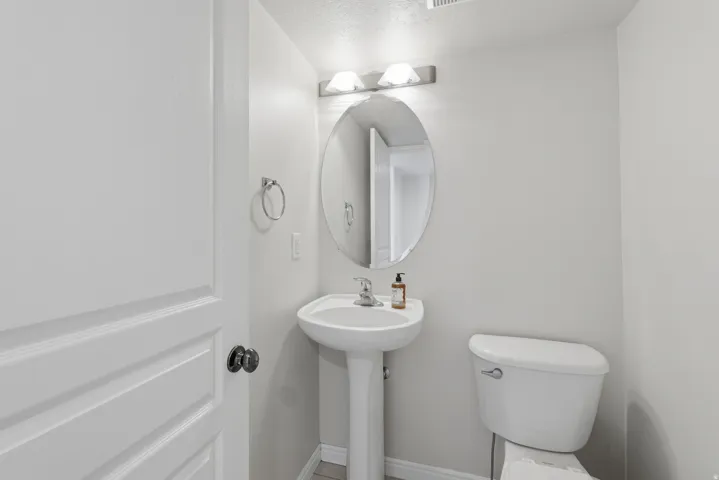 Pedestal sink with an oval mirror, wall-mounted vanity light, and a white toilet