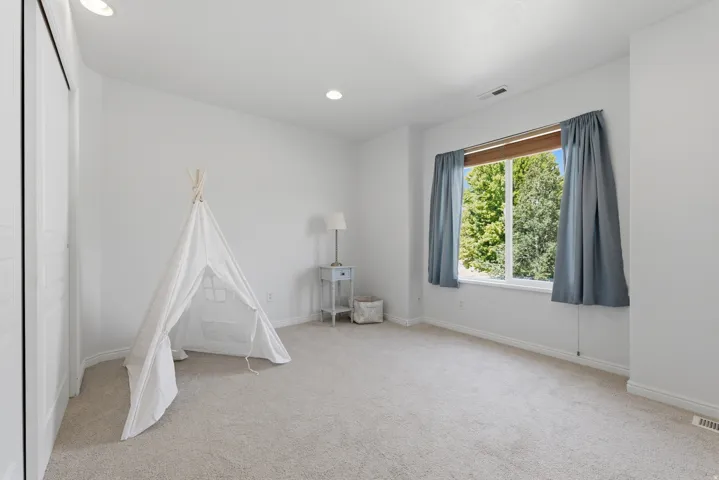 Bright room featuring a large window with exterior tree scenery, recessed lighting, neutral carpet flooring, and white bifold closet doors