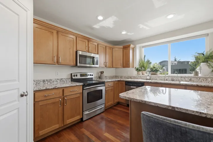 Kitchen featuring wood cabinetry, stainless steel appliances, granite countertops, and hardwood flooring