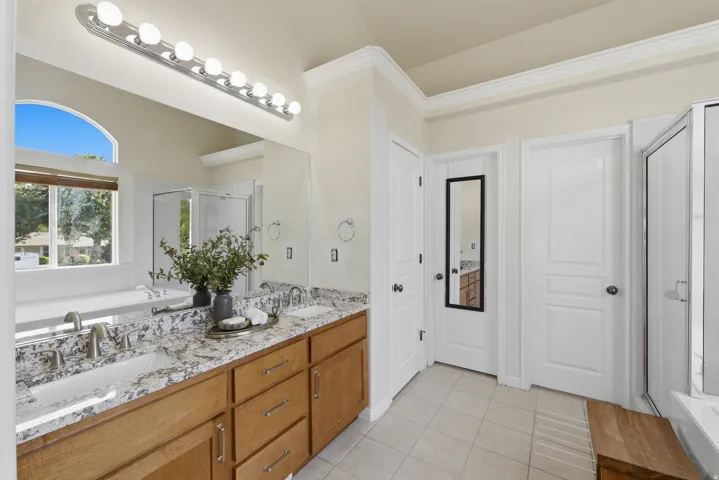 Bathroom featuring a double vanity with stone countertops, a large soaking tub, and a separate glass-enclosed shower