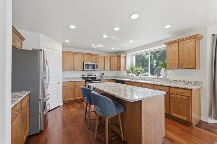 Spacious kitchen featuring warm wood cabinetry, light-toned countertops, stainless steel appliances, a center island with seating, and recessed lighting