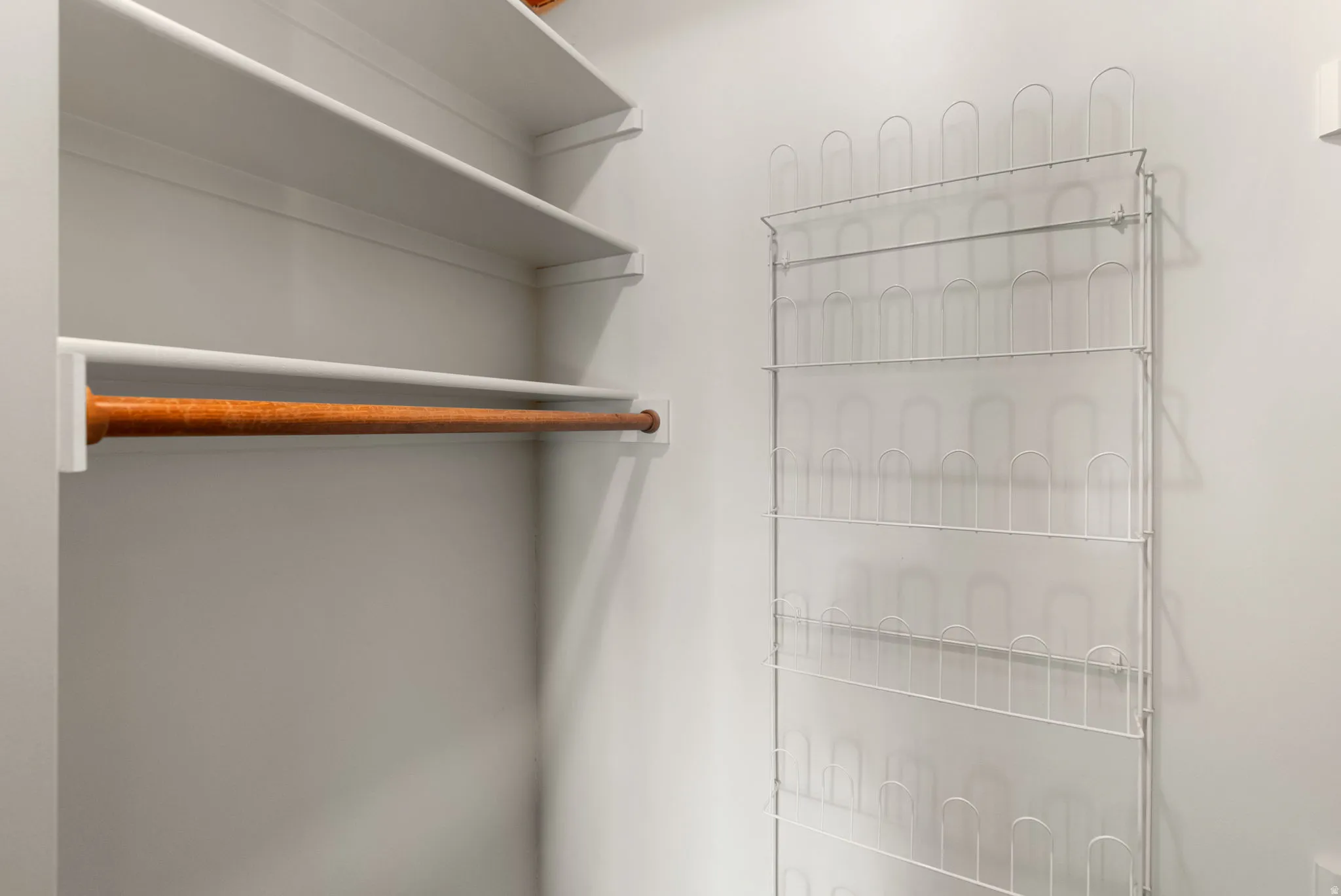 Closet interior featuring a wooden hanging rod, white shelving, and a wall-mounted wire shoe rack
