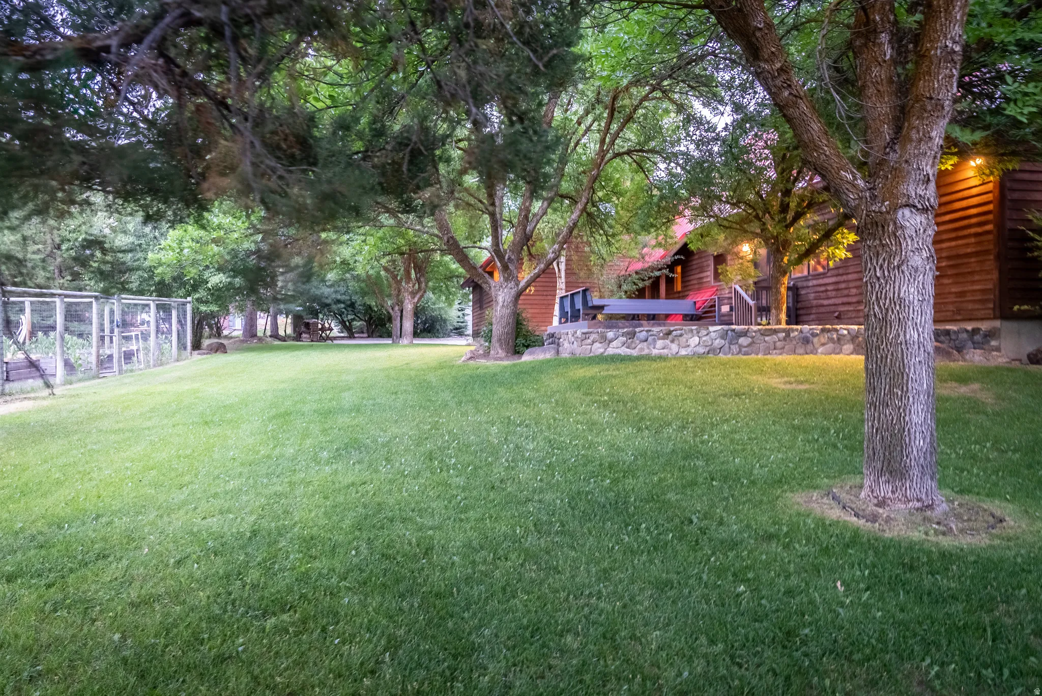 Expansive lawn area featuring mature trees and a stone-clad retaining wall