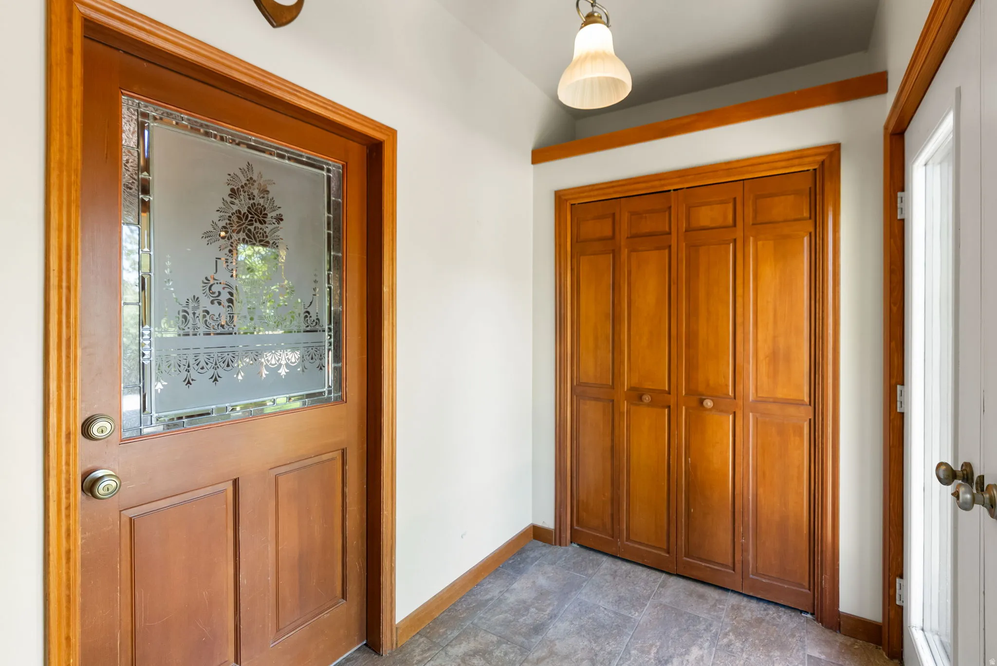 Entryway featuring a wood-panel door with decorative frosted glass, bi-fold closet doors, and tile flooring