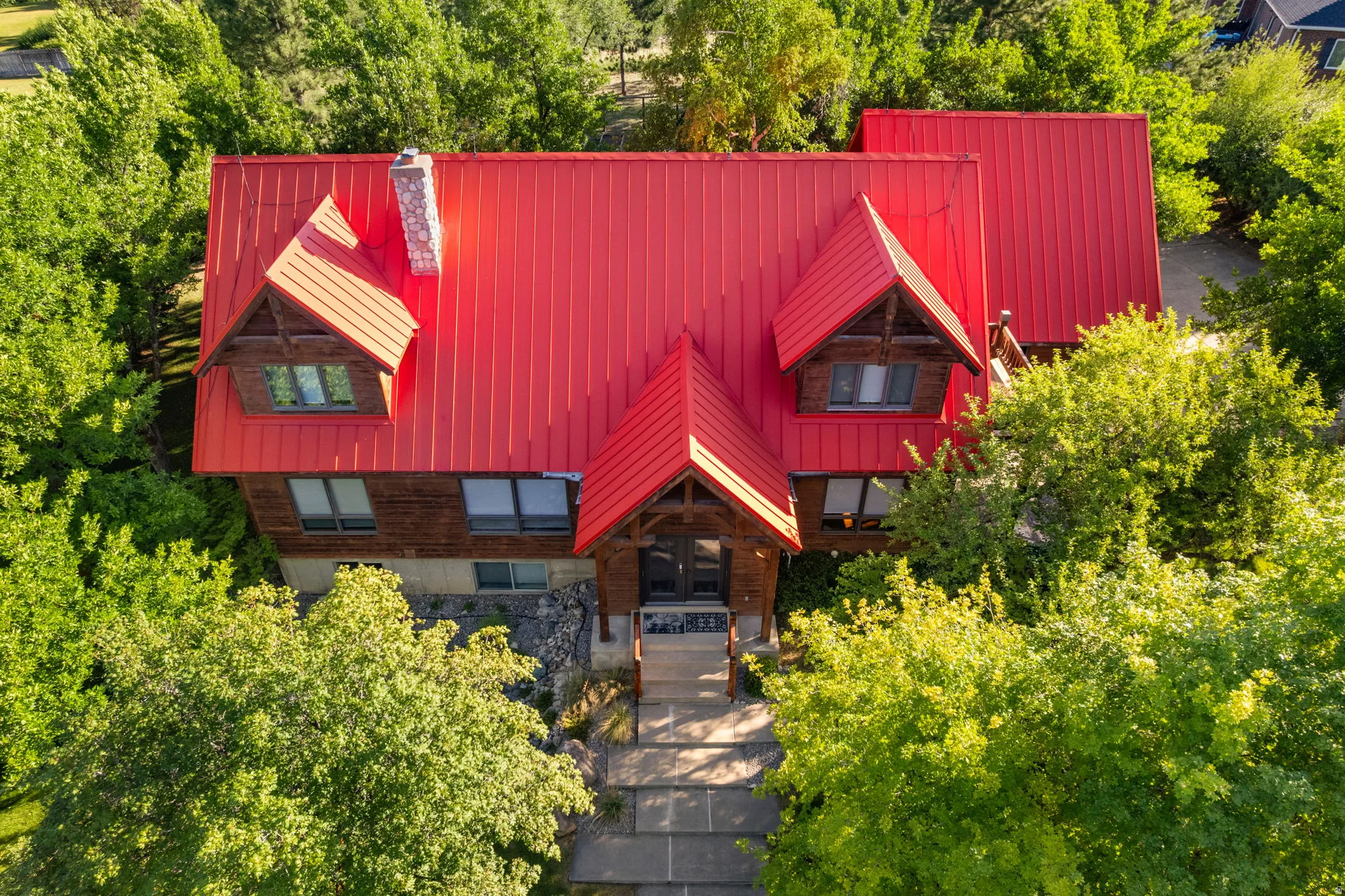 Wood-clad exterior with a prominent red metal roof, dormer windows, and a stone chimney