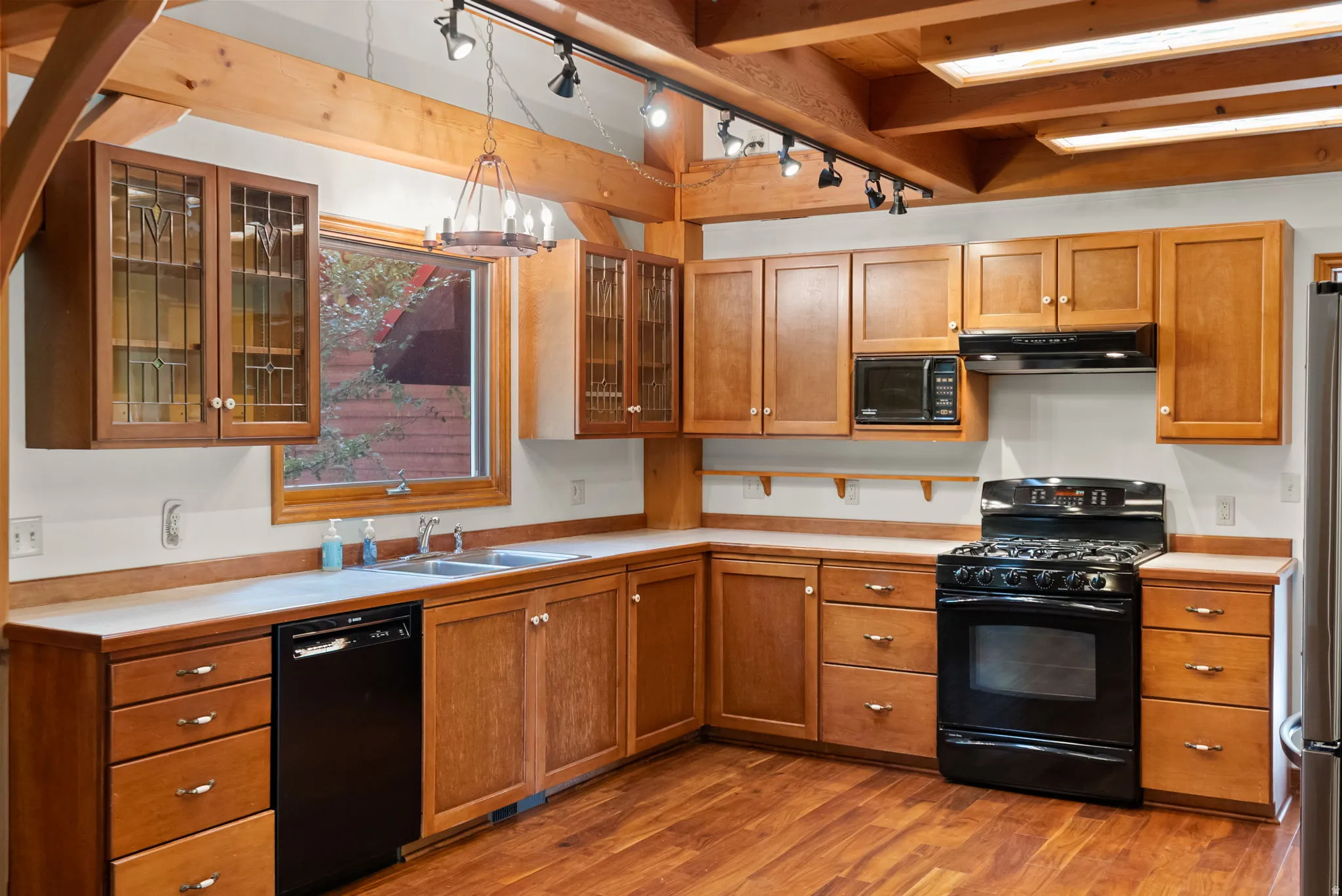 Spacious kitchen featuring wood-finish flooring, natural wood cabinetry, a double basin sink, and a full suite of black appliances