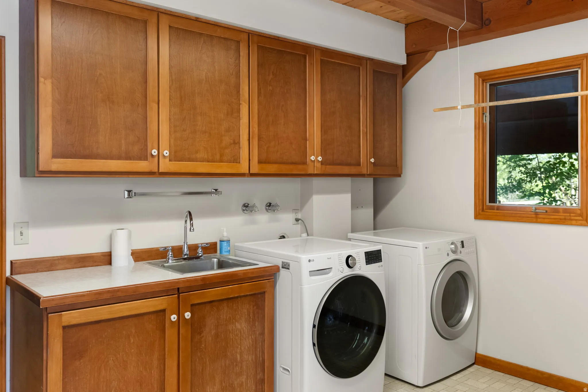 Laundry room featuring wood cabinetry, integrated utility sink, and wood-beam ceiling details