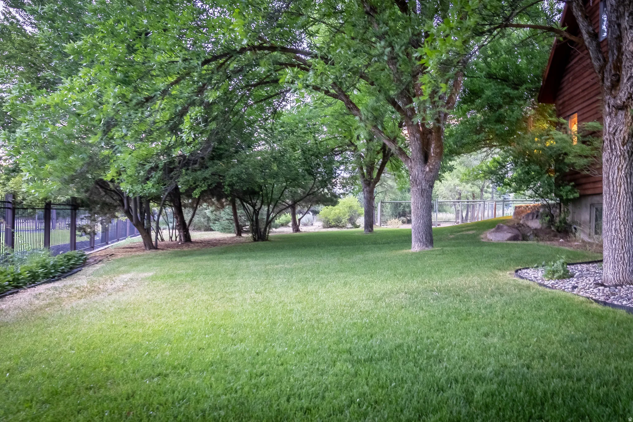 Expansive lawn area featuring mature trees, a privacy fence, and a rock bed perimeter