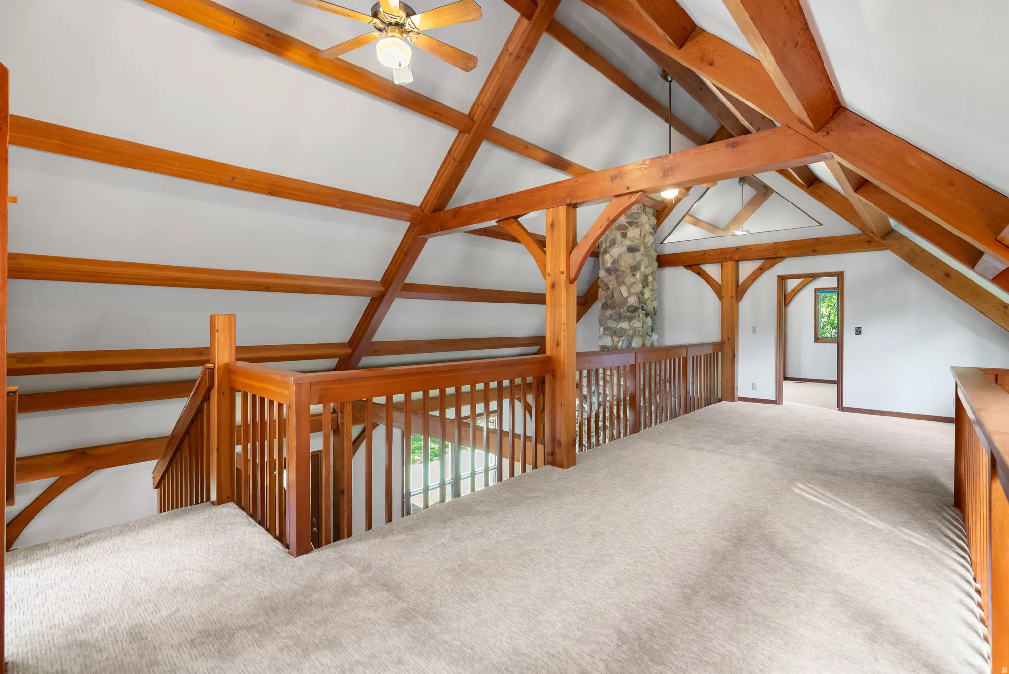Open loft area featuring exposed timber beams, vaulted ceiling, and light-toned carpeting