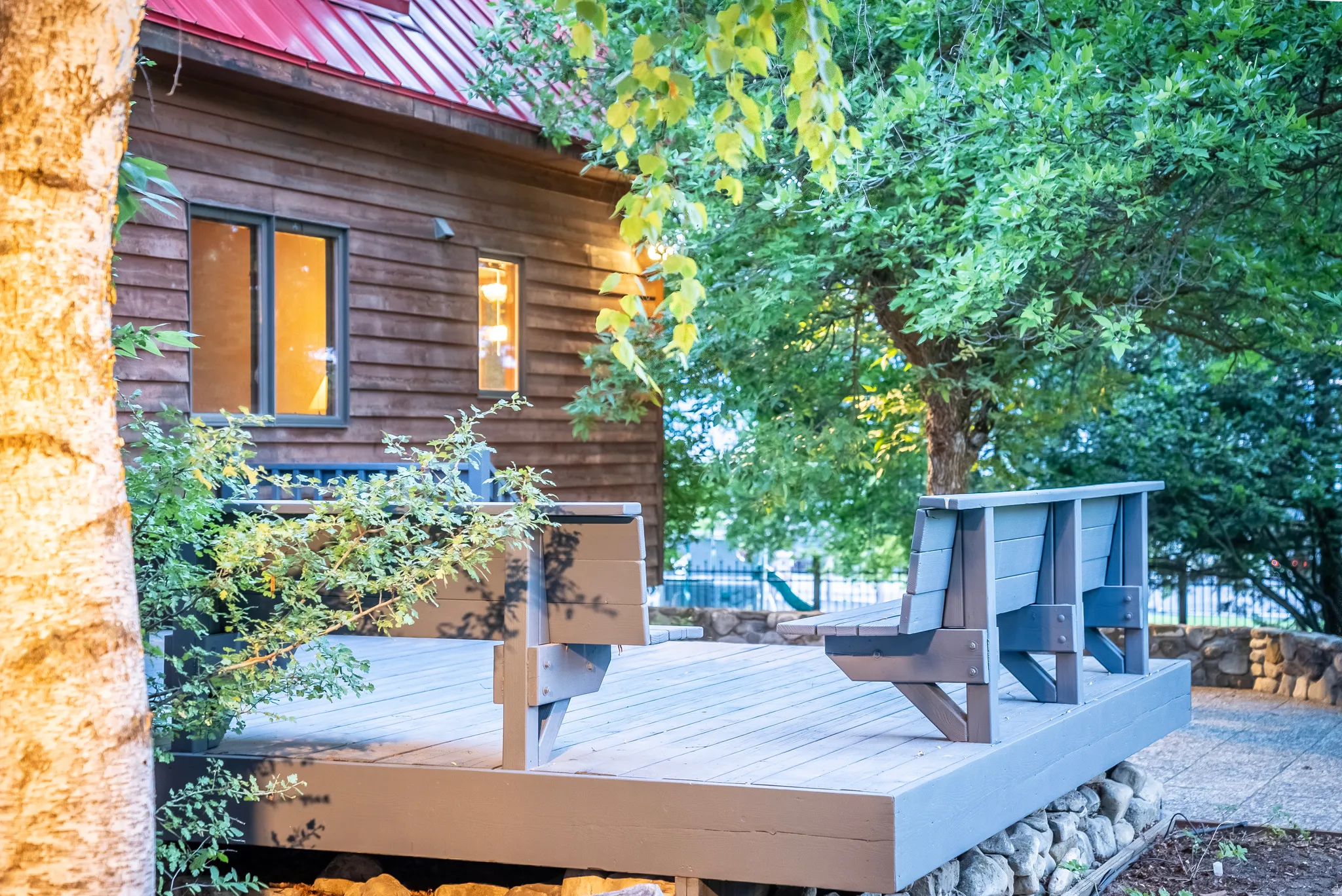 Outdoor deck area featuring built-in seating, a stone retaining wall, and mature landscaping
