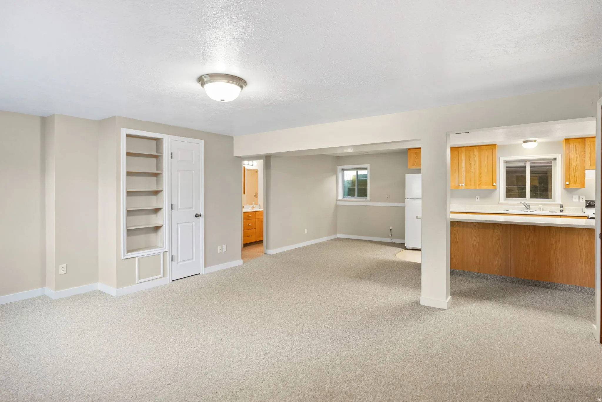 Spacious open-concept living area featuring light-toned carpeting, built-in shelving, and a neutral wall palette