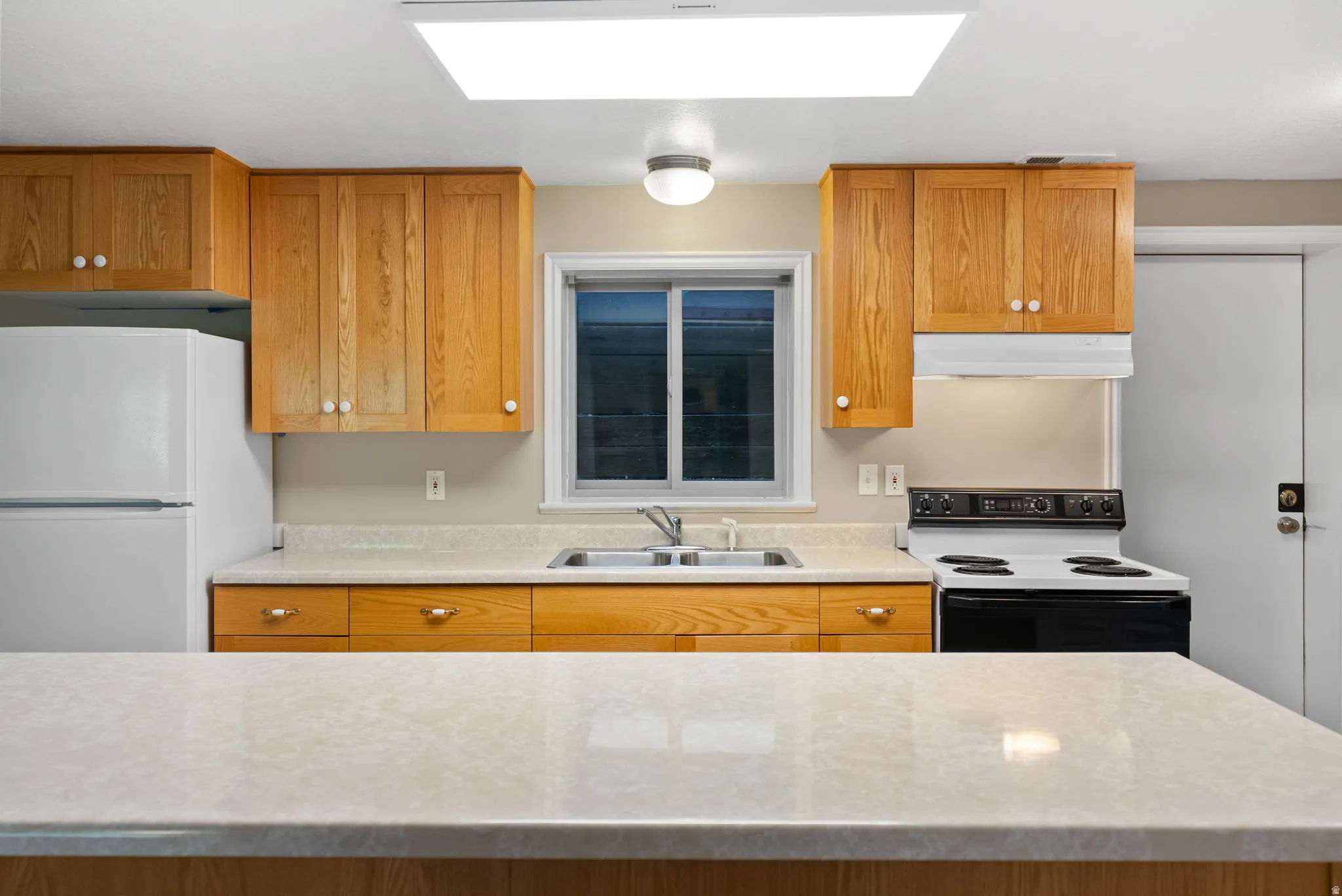 Kitchen featuring wood cabinetry, light-colored countertops, a double basin sink, and a white electric range with an overhead vent