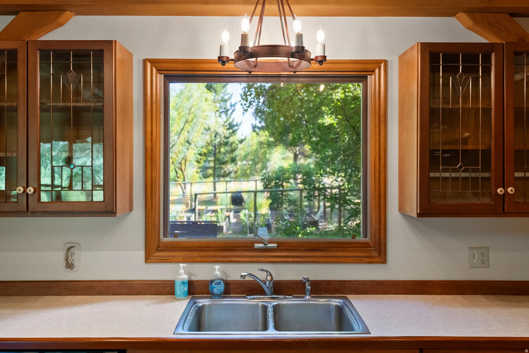 Kitchen window with wood trim, dual-basin stainless steel sink, and light-colored countertop