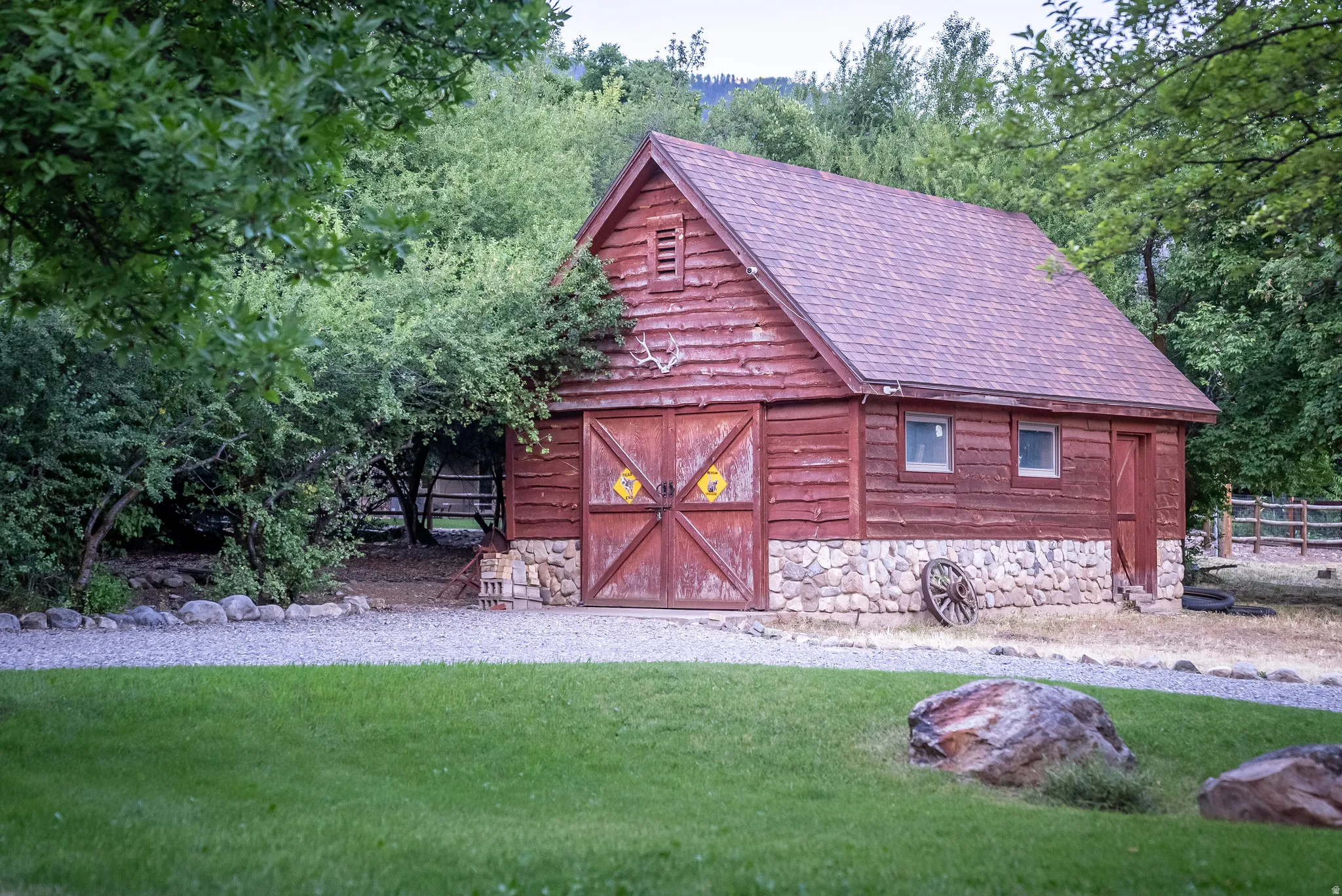 Rustic outbuilding featuring red wood siding, a stone foundation, double barn doors, and an asphalt shingle roof