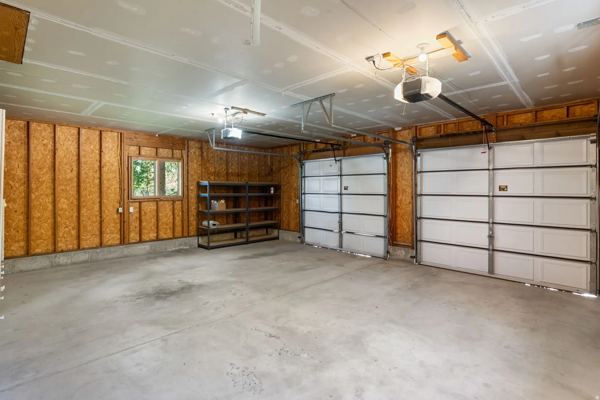 Spacious two-car garage featuring a concrete floor, exposed wood-paneled walls, and a window for natural light