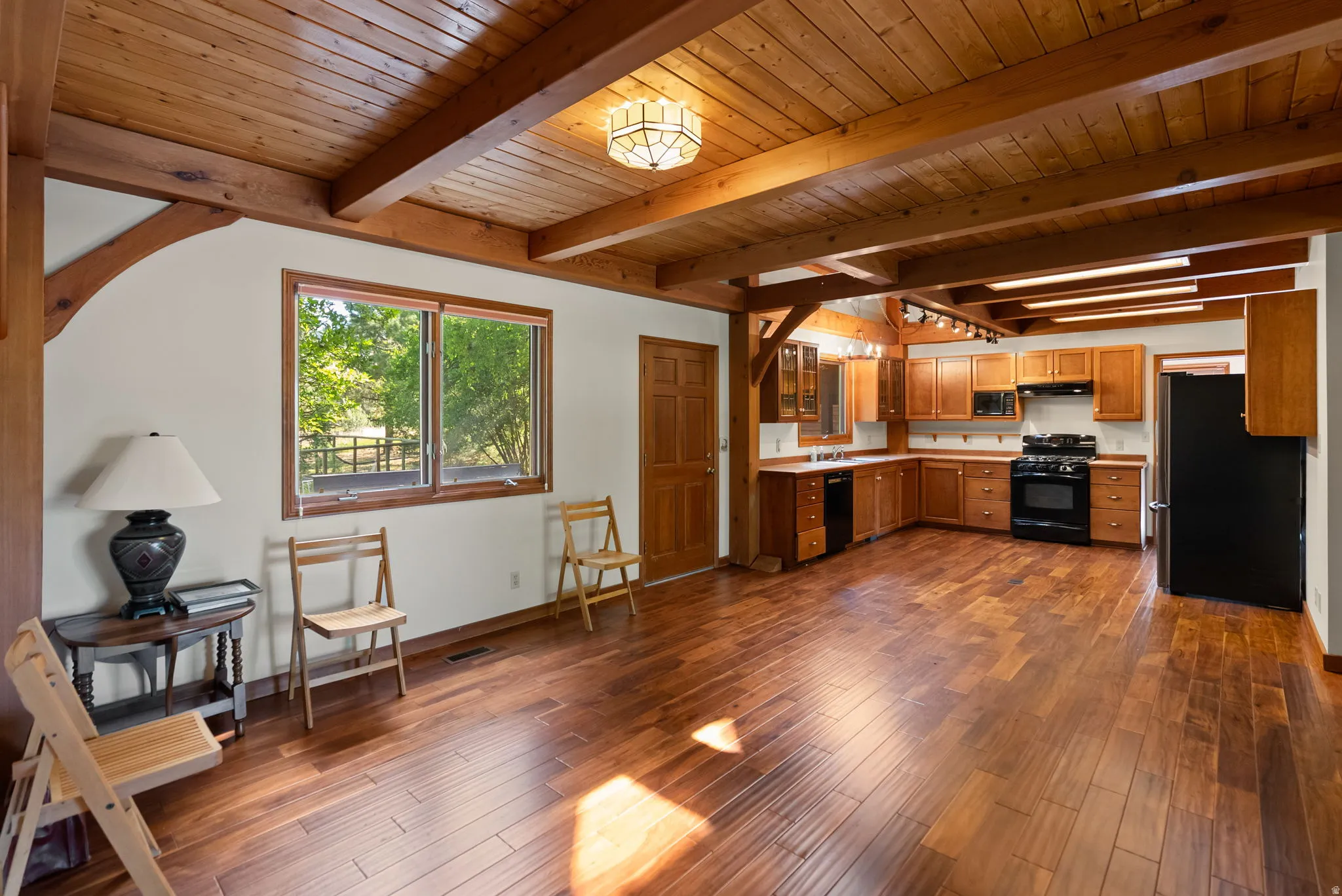 Open-concept living space featuring wood-finish flooring, exposed wood beam ceiling, and a kitchen with wood cabinetry