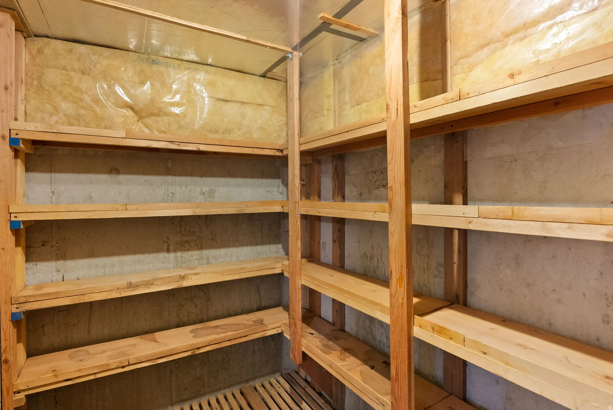 Dedicated storage room featuring extensive wood shelving, concrete walls, and visible insulation
