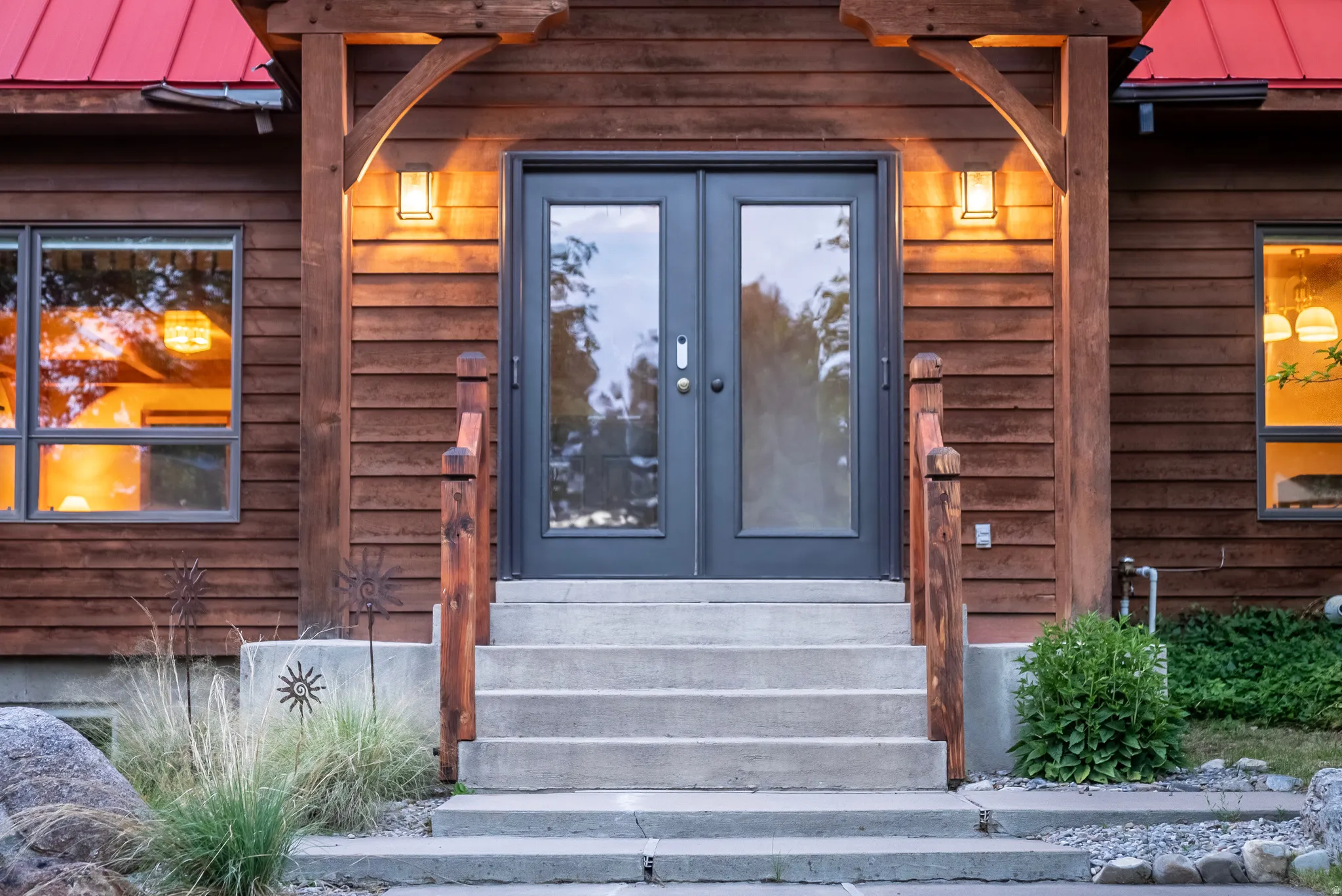 Entryway featuring dark-framed double doors with glass panels, concrete steps, and wooden handrails