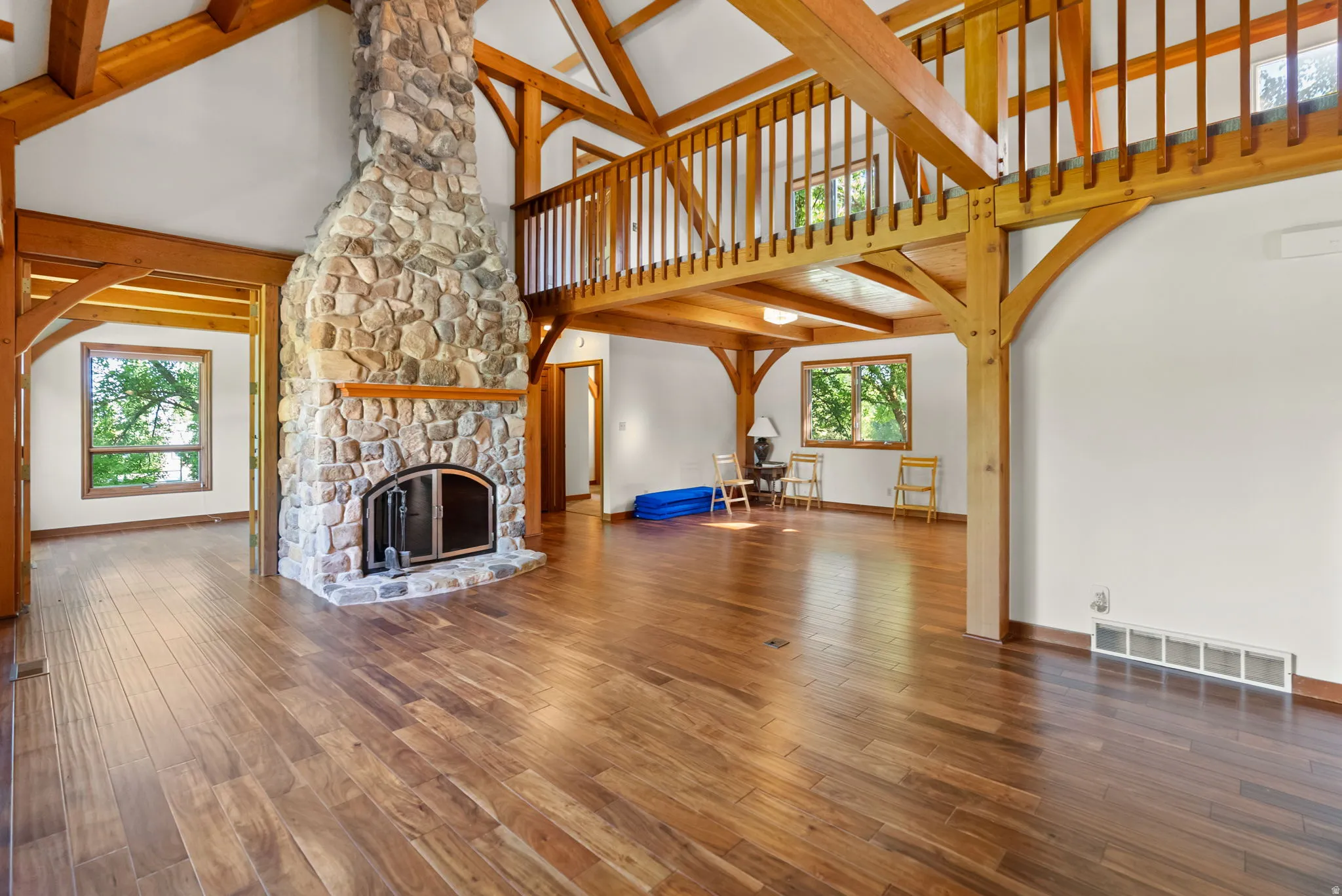 Great room featuring a stone fireplace with a raised hearth, wood-finish flooring, exposed wood beams, and a second-story wood railing