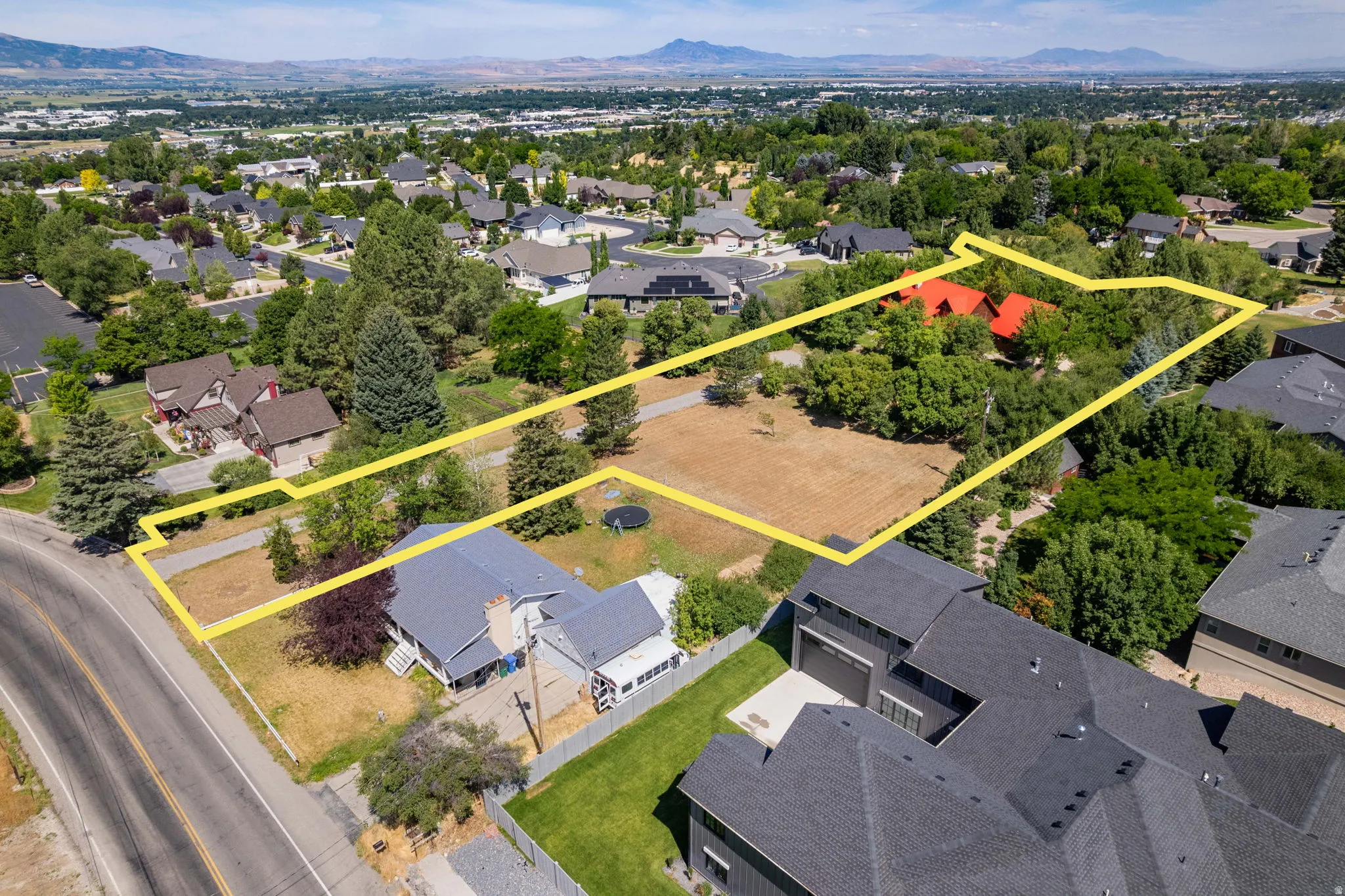 Expansive property featuring a substantial land parcel, established perimeter fencing, mature trees, and a mountain range backdrop