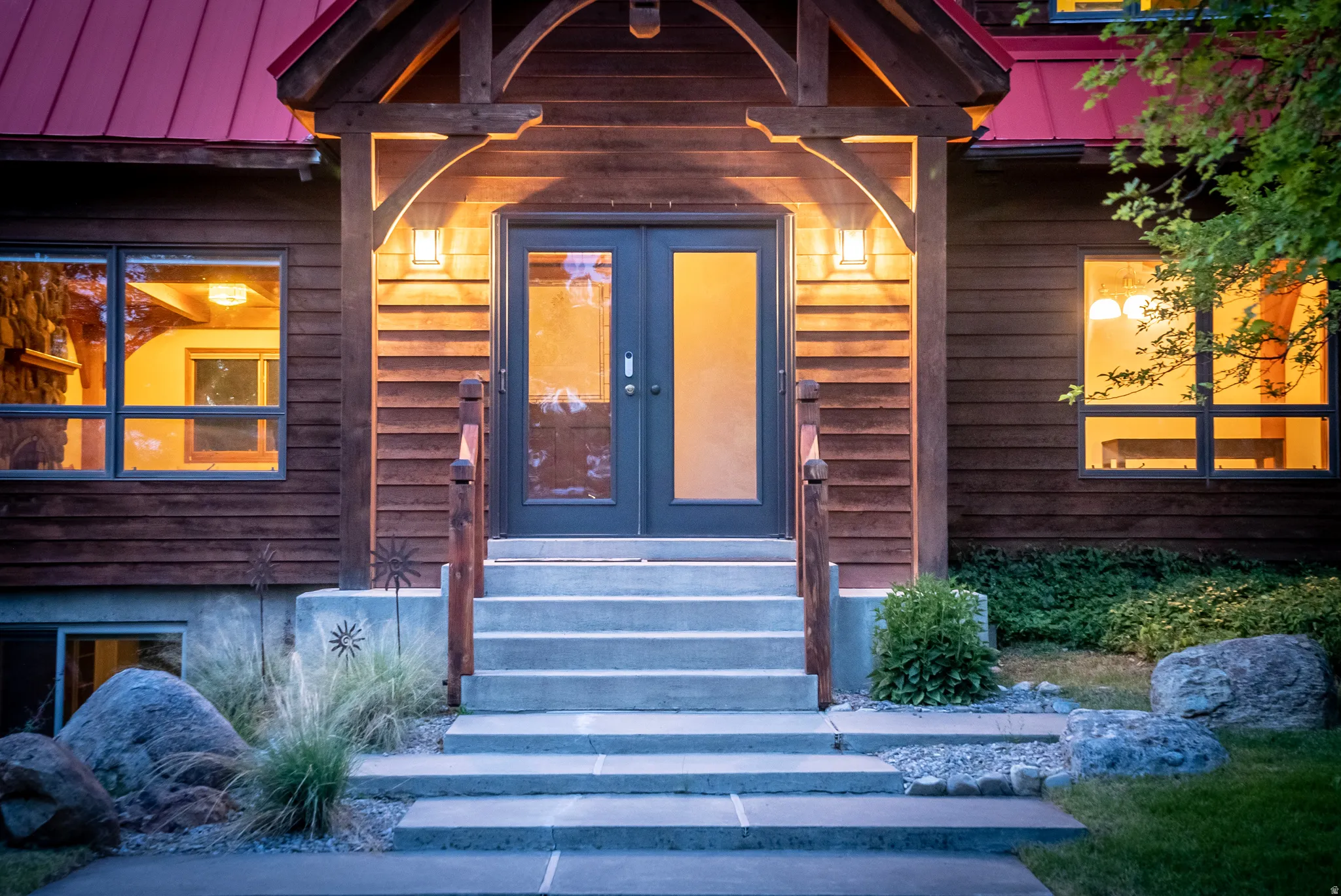 Wood-sided exterior featuring a red metal roof and concrete steps leading to double-panel glass entry doors