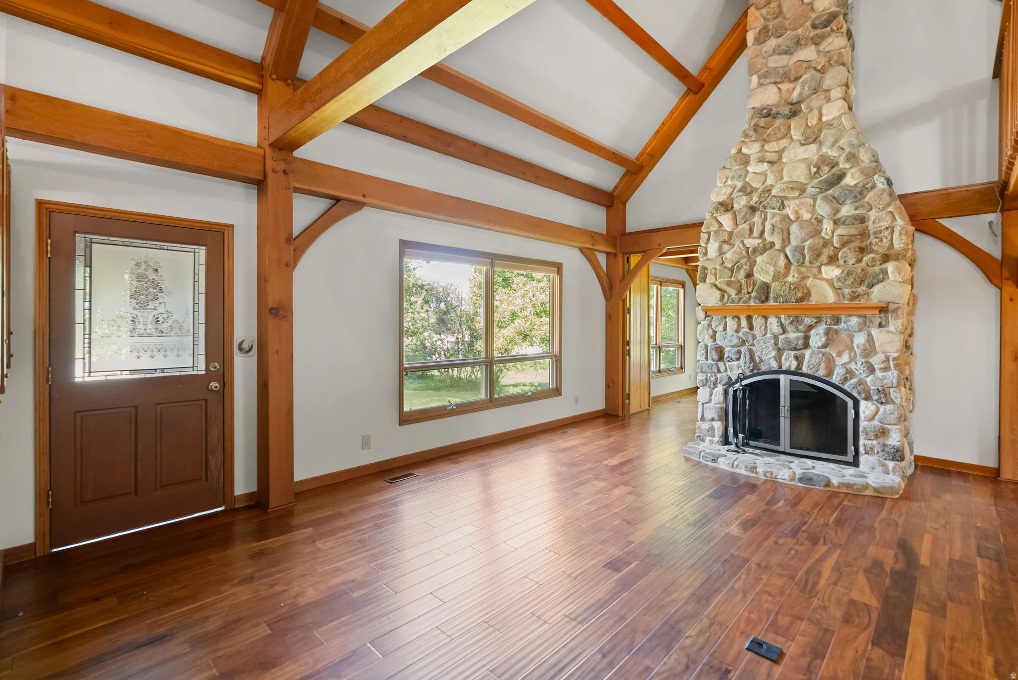 Spacious living area featuring a floor-to-ceiling stone fireplace, vaulted ceilings with exposed wood beams, and rich wood-finish flooring