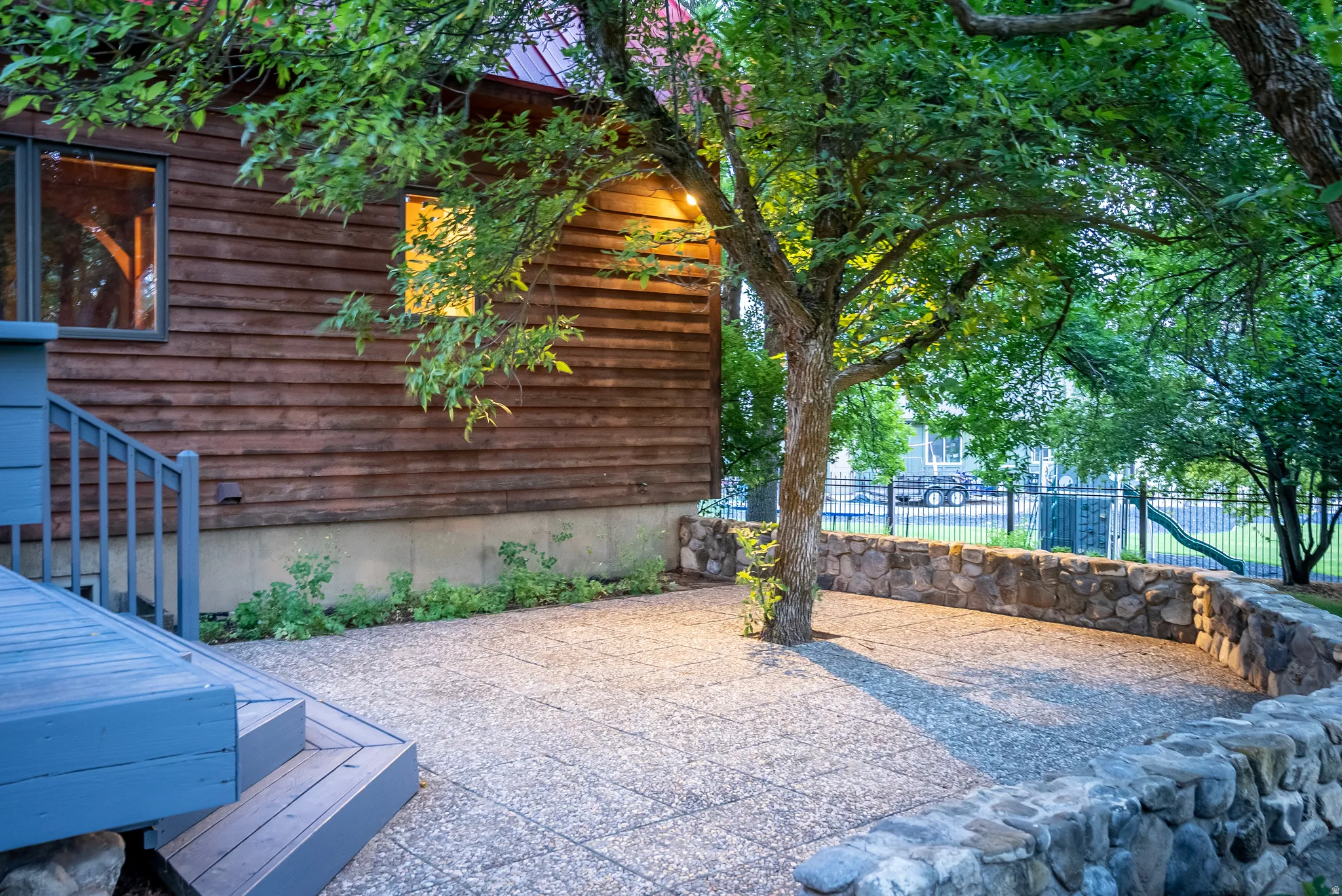 Outdoor patio featuring aggregate paving, a curved stone retaining wall, and mature tree landscaping