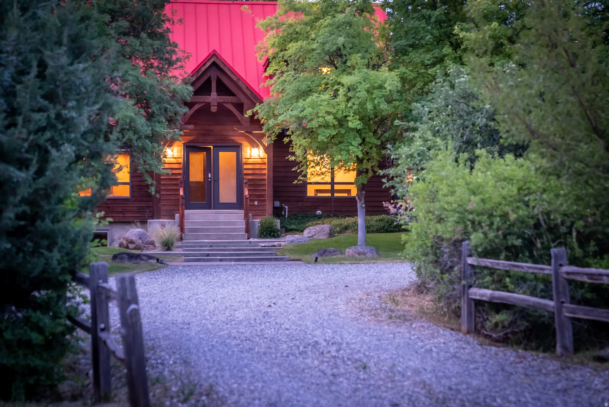 Timber-frame home featuring a red metal roof, covered front porch, double entry doors, and mature surrounding foliage