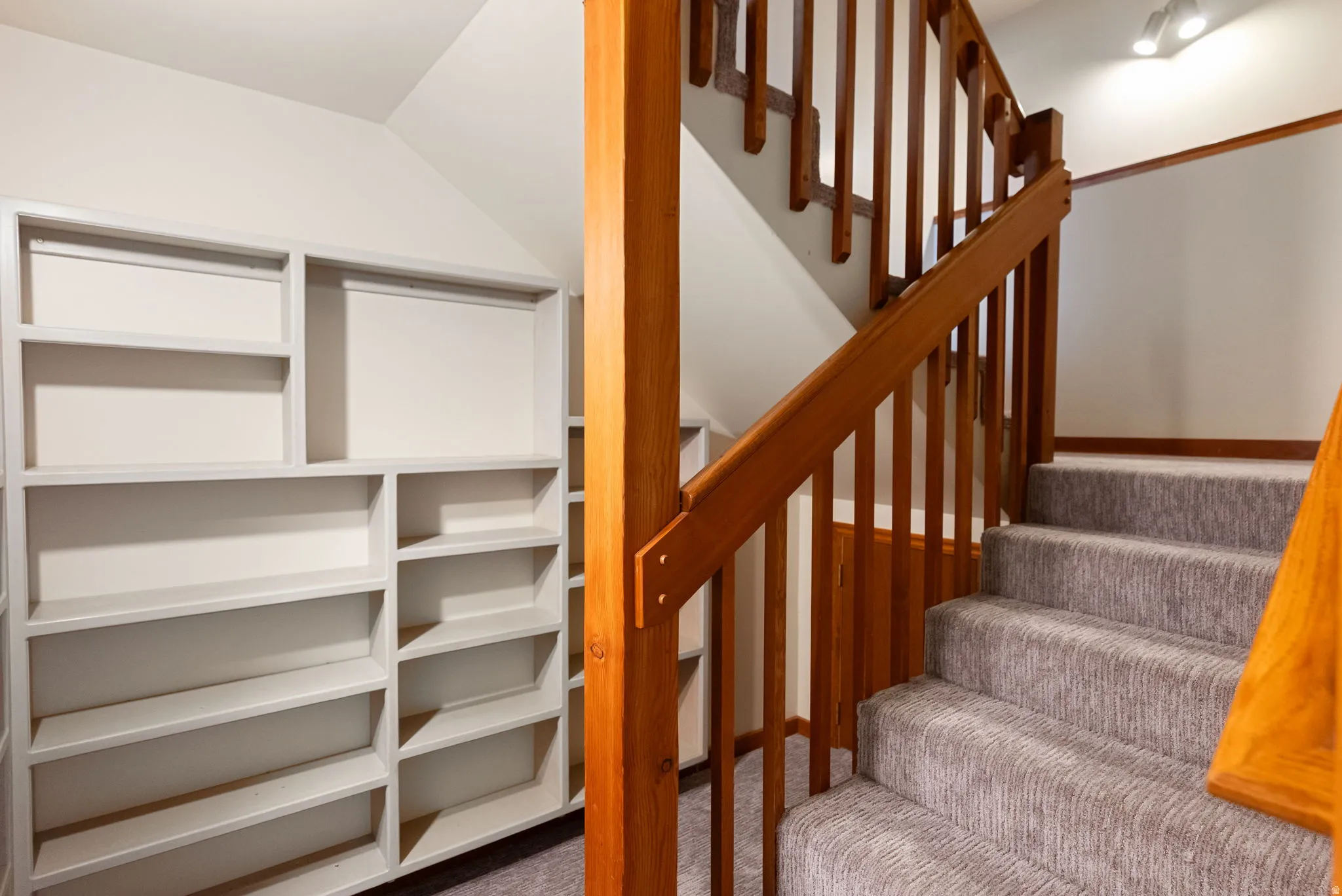 Custom built-in shelving and a carpeted staircase with wood railings