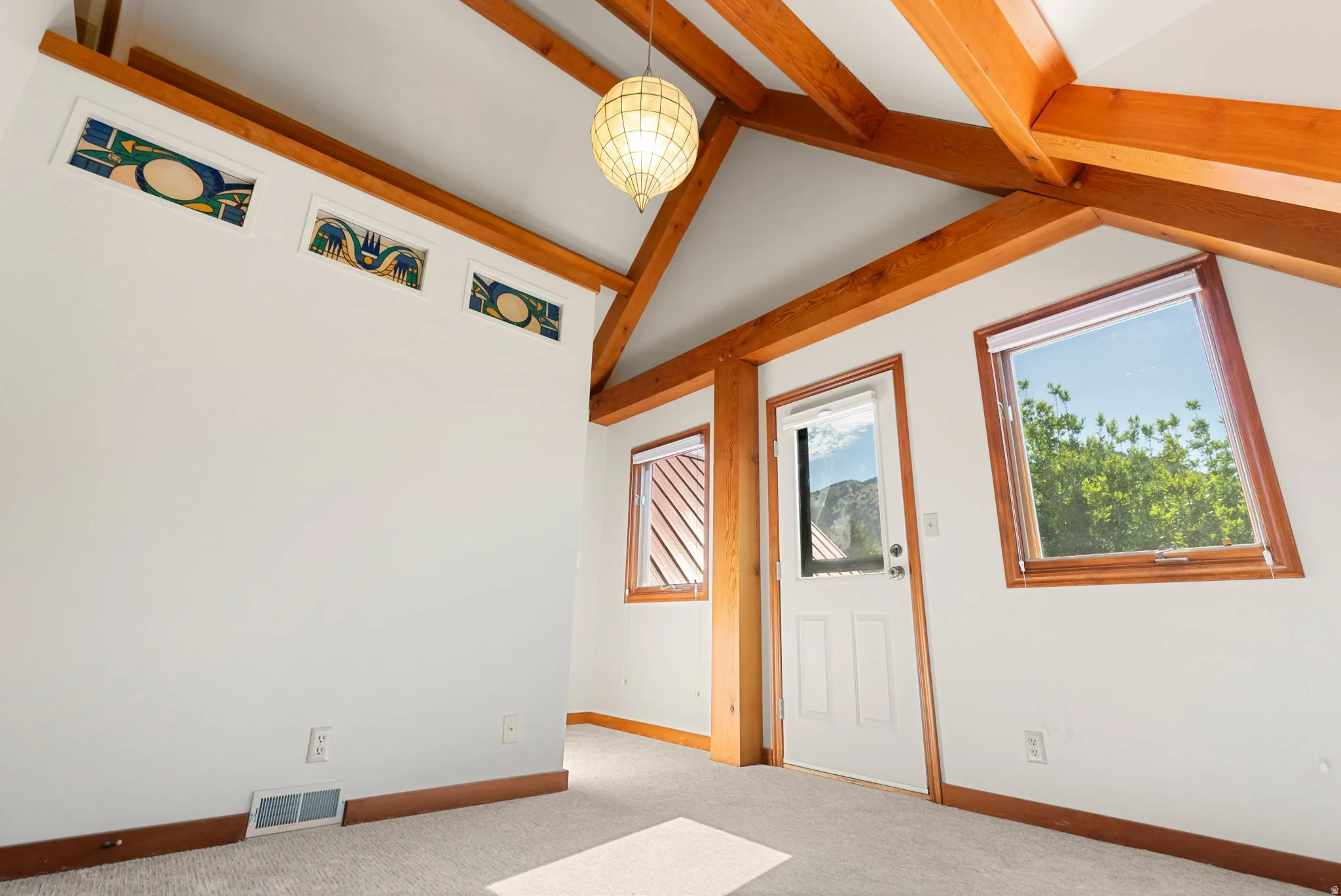 Vaulted ceiling with exposed wood beams, stained glass transom windows, wood-trimmed windows, a ceiling-mounted light fixture, and carpet flooring
