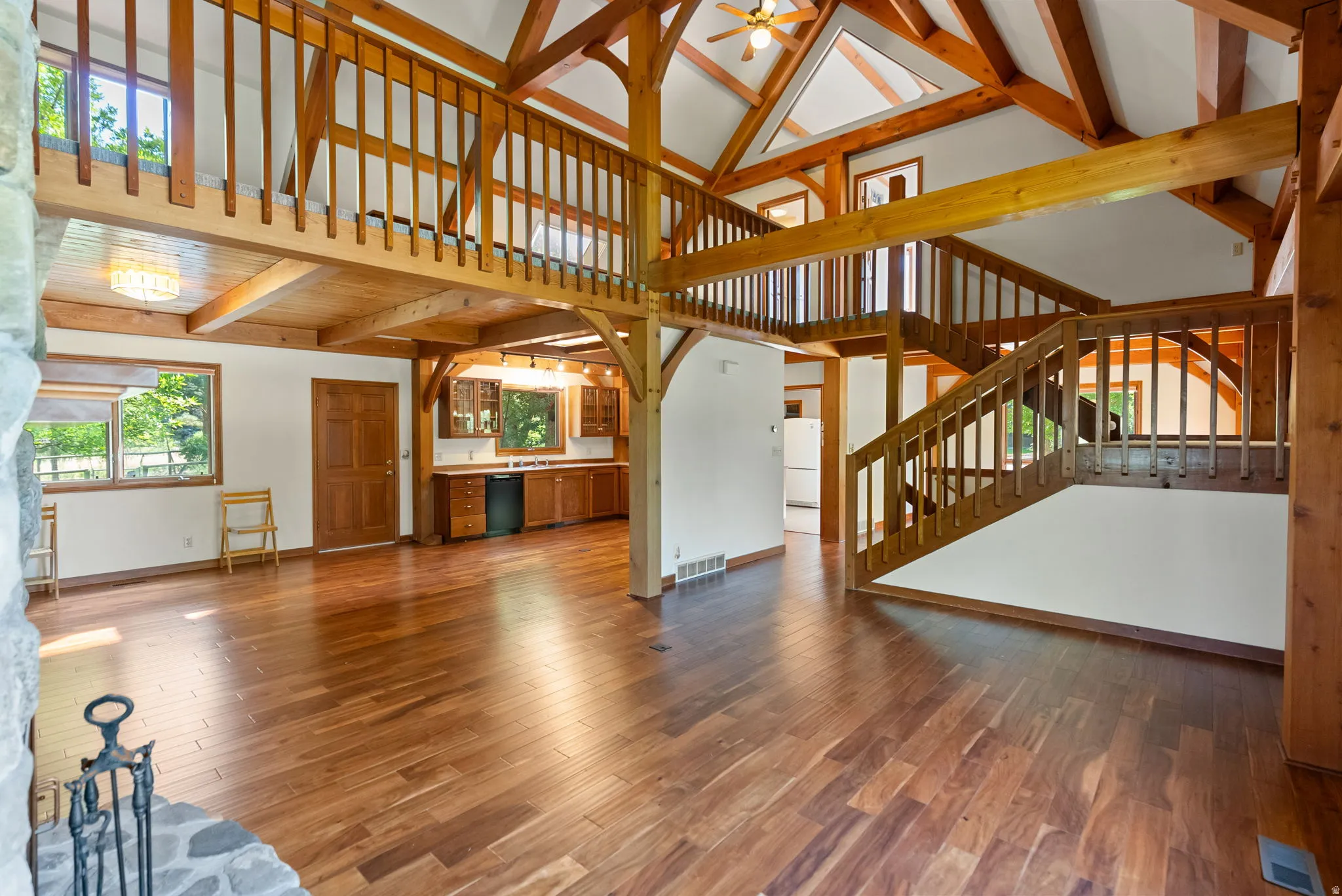 Vaulted ceilings with exposed wood beams, wood-finish flooring, and a stone fireplace surround