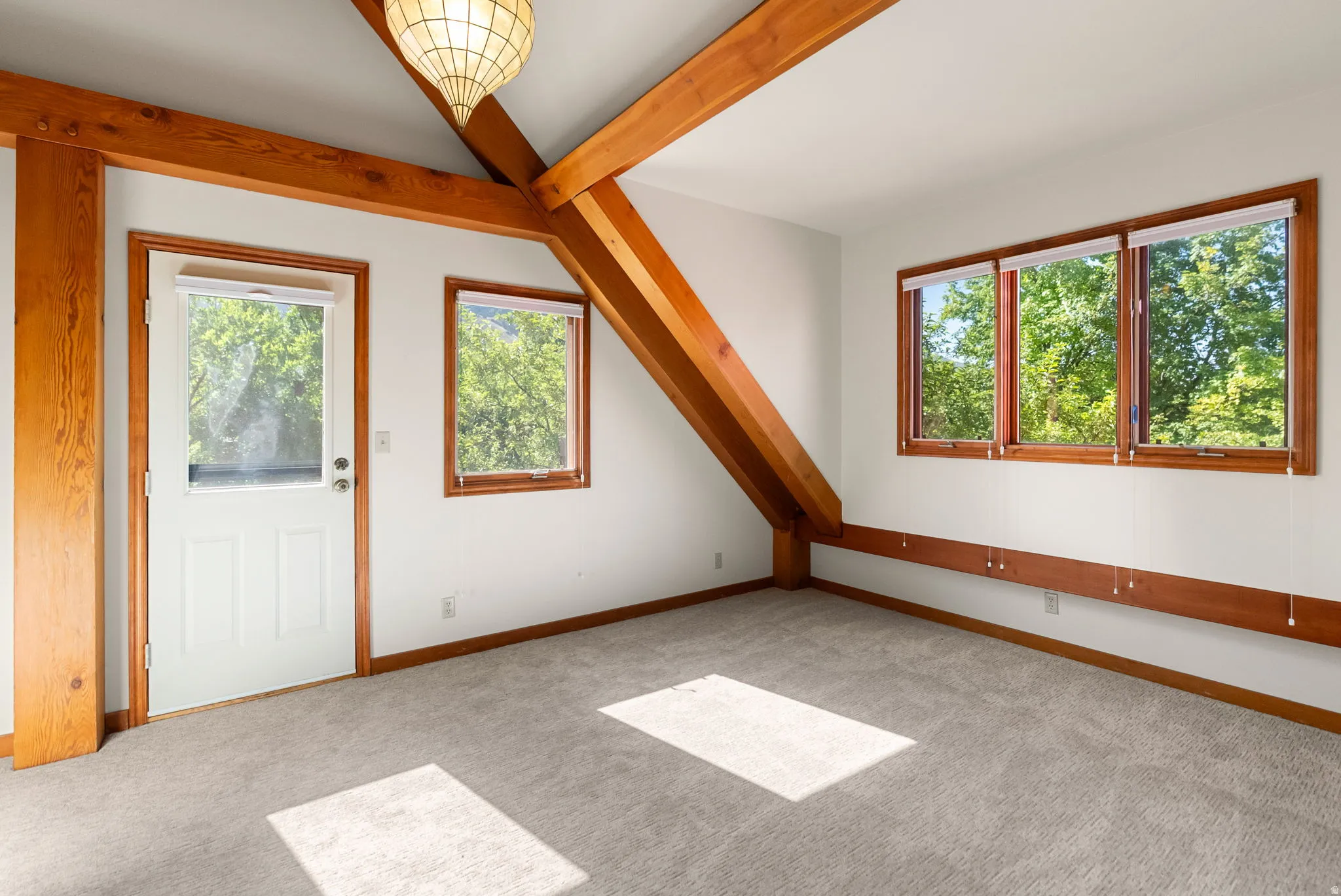 Exposed wood beams and trim accents a room featuring multiple windows, a paneled door, and neutral carpeting