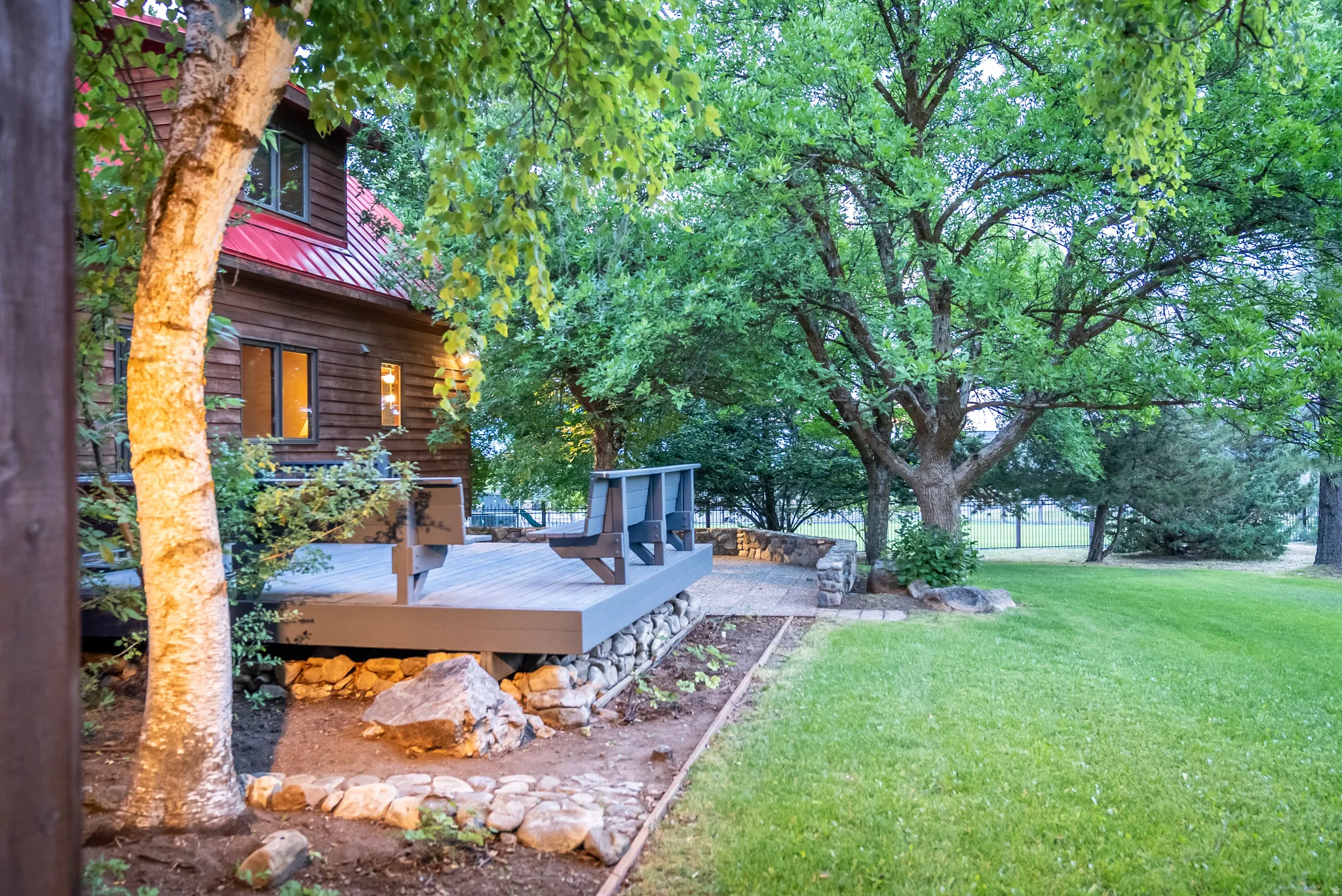 Exterior featuring wood siding, a red metal roof, a composite deck, stone hardscaping, and mature trees