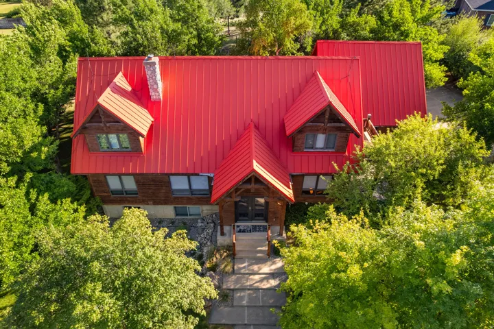 Wood-clad exterior with a prominent red metal roof, dormer windows, and a stone chimney