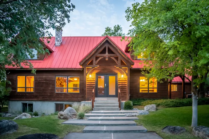 Wood-sided residence featuring a vibrant red metal roof and a prominent stone chimney