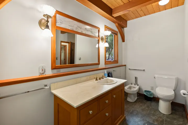 Bathroom featuring a wood-finish vanity with an integrated sink and light-toned countertop, a large wood-framed mirror, and a window with wood trim