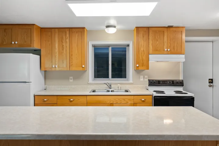 Kitchen featuring wood cabinetry, light-colored countertops, a double basin sink, and a white electric range with an overhead vent