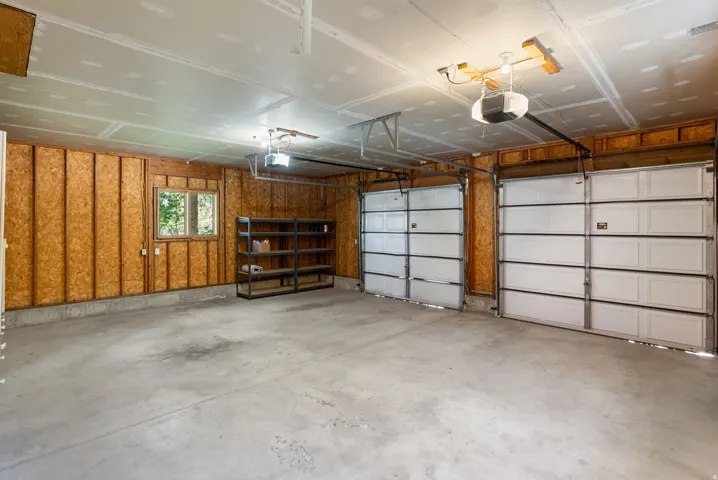 Spacious two-car garage featuring a concrete floor, exposed wood-paneled walls, and a window for natural light