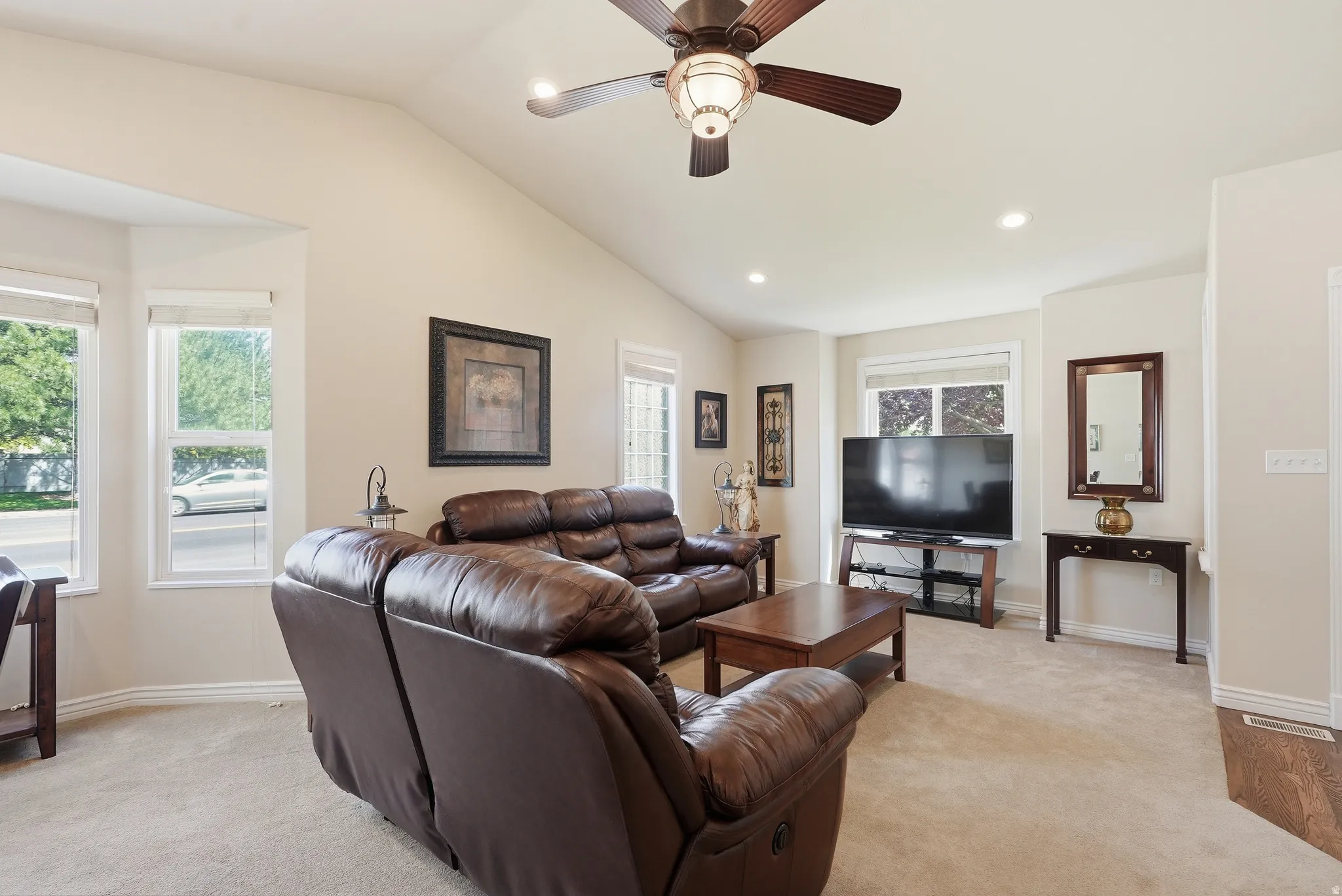 Spacious living area featuring vaulted ceilings, recessed lighting, carpet flooring, multiple windows, and a ceiling fan