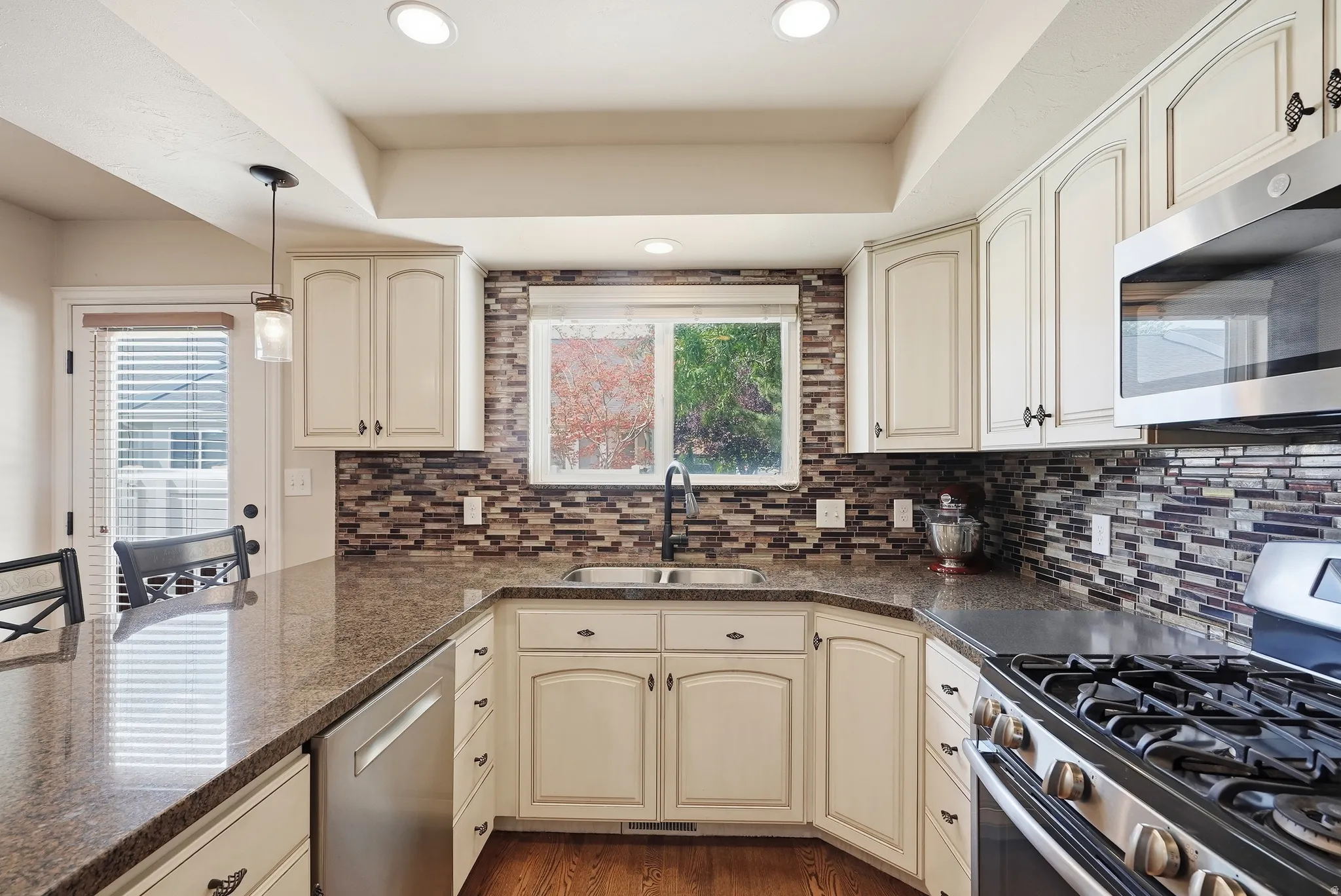 U-shaped kitchen featuring stone countertops, a mosaic tile backsplash, stainless steel appliances, white cabinetry, and recessed lighting